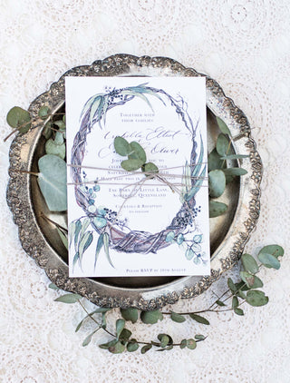 Twist gum tree branches in a wreath on a wedding invitation. Vintage props in background.