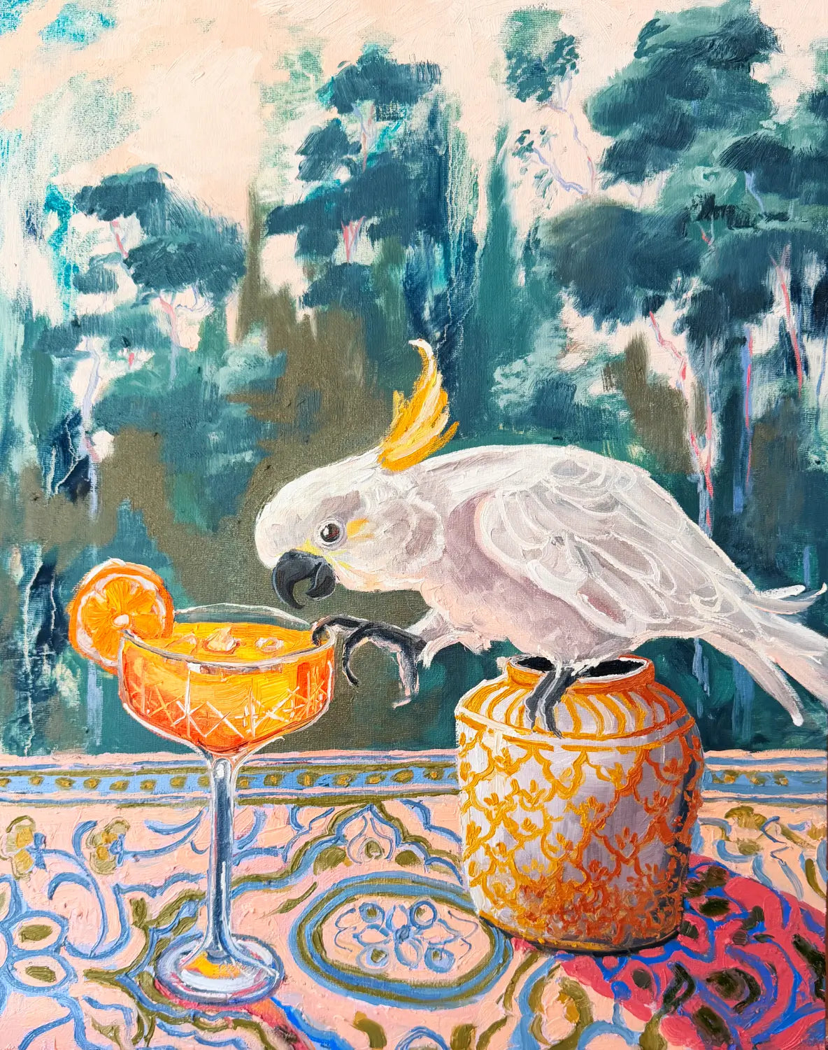 A cheeky still life painting. A colourful painting of a white cockatoo perched on a patterned table next to an orange cocktail glass and a decorative vase, with a painted Australian forest background.