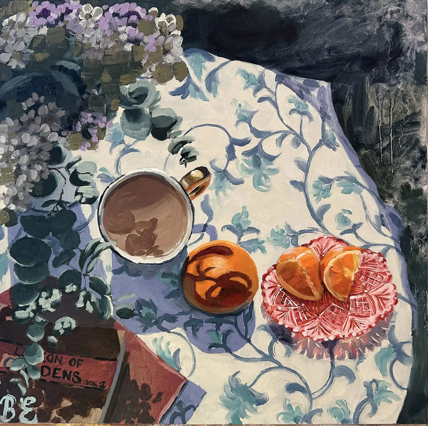 Still life with a cup of coffee, oranges, and flowers on a patterned tablecloth.