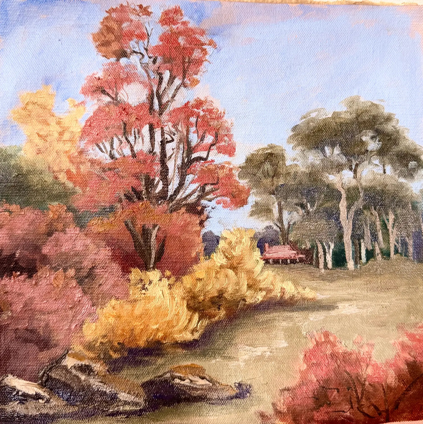 An oil painting of an autumn landscape featuring vibrant red, pink, and yellow trees, a dirt path, rocks in the foreground, and a small Australian timber slab cottage in the background under a pale blue sky.